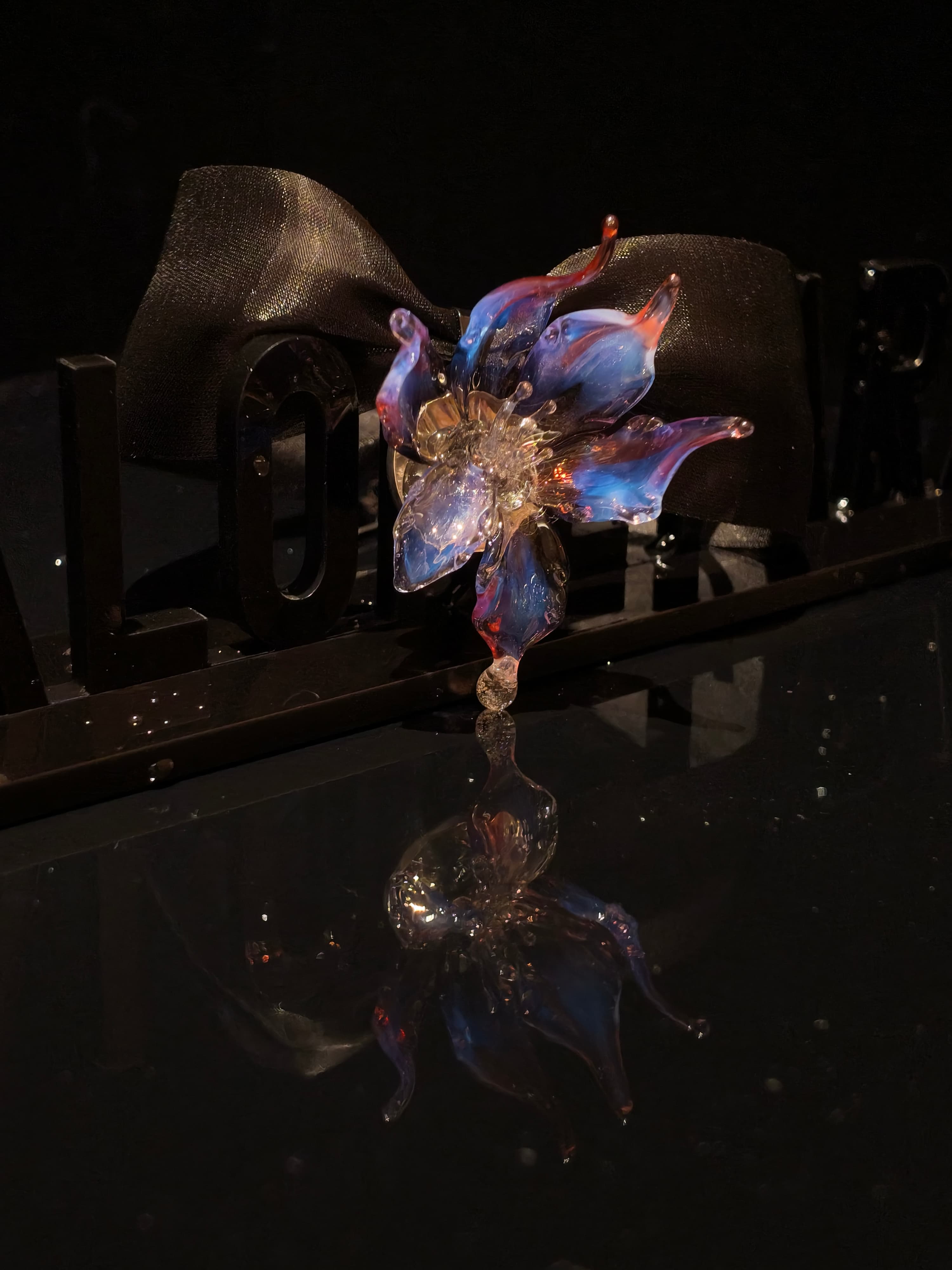 Close-up of handcrafted purple blue Liuli glass orchid floral pendant, deep purple and blue petals with crystal clear details against black background