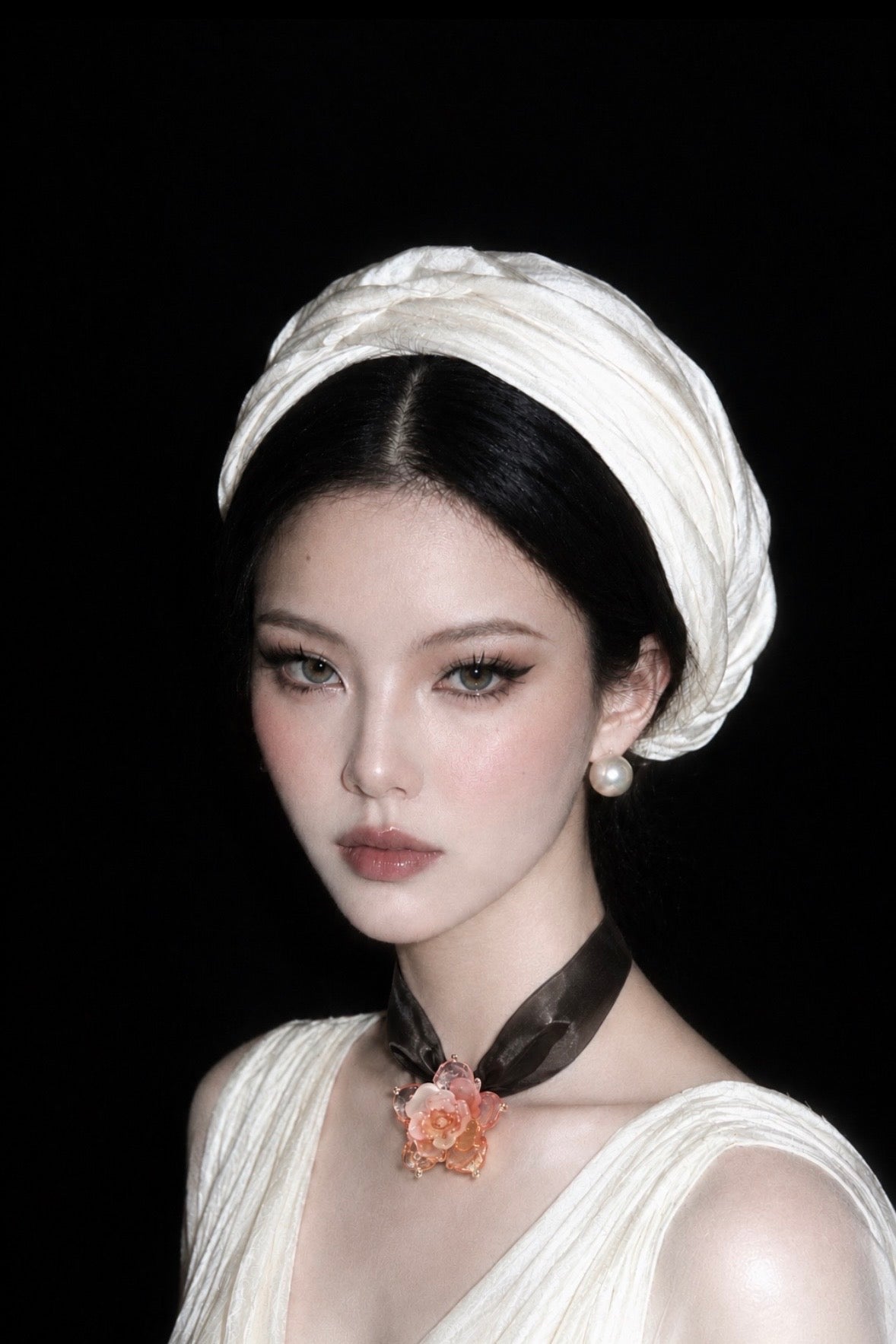 Model wearing a pink rose Liuli necklace on a black ribbon with a white V-neck dress and white headwrap.