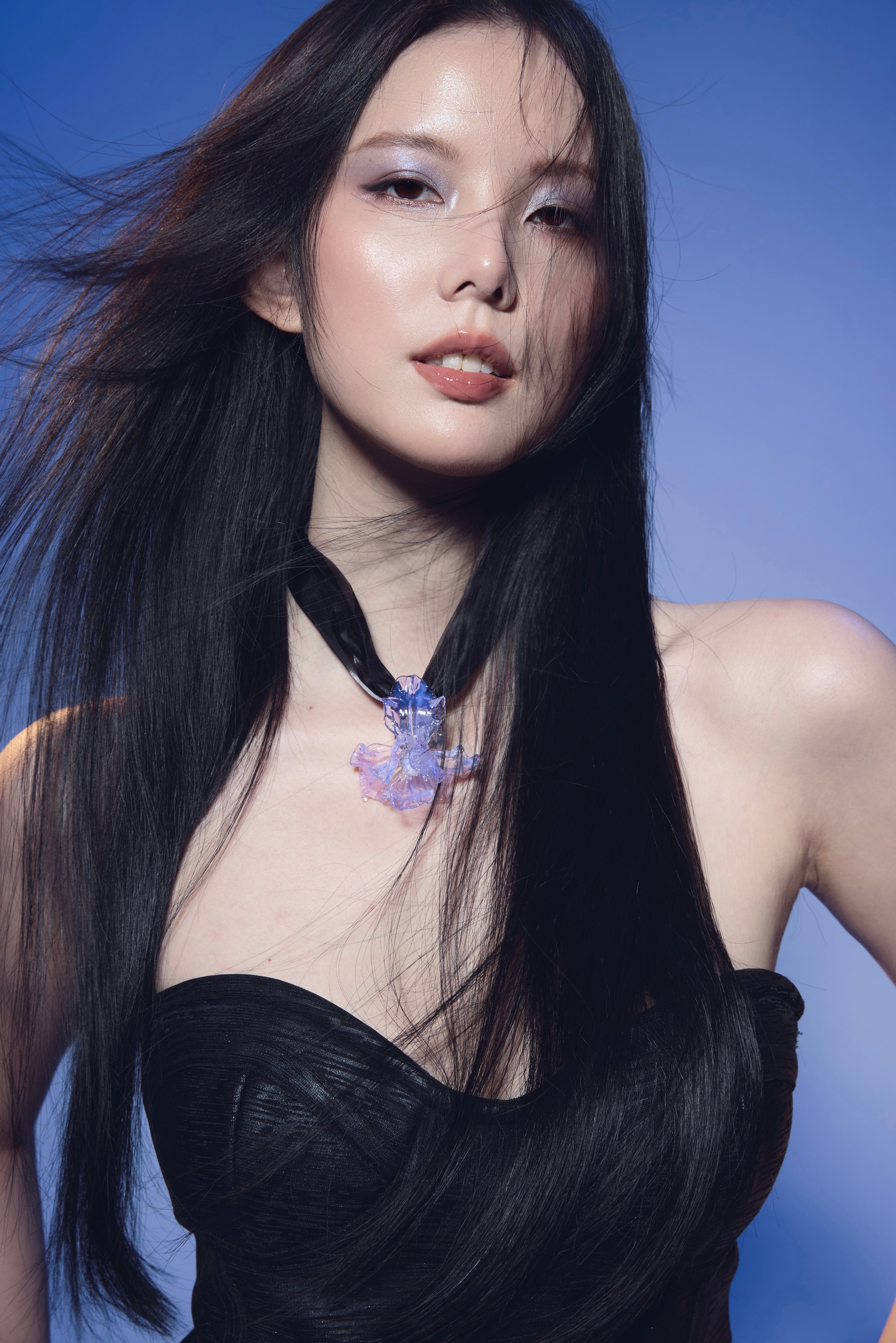 Young woman wearing Enchantress Purple-blue Liuli Glass necklace, styled in a black strapless top against a deep purple background
