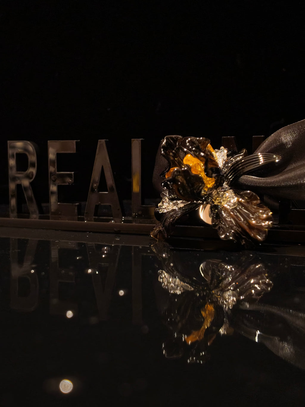 Close-up of handcrafted black gold Liuli glass iris floral pendant, deep black petals with gold accents and crystal clear details against black background