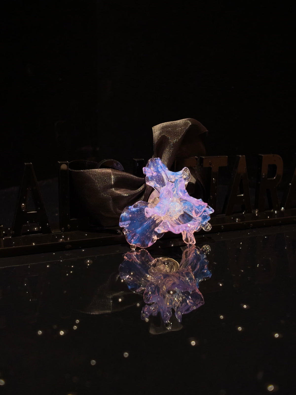 Close-up of handcrafted purple Liuli glass iris floral pendant, deep purple petals with crystal clear details against black background