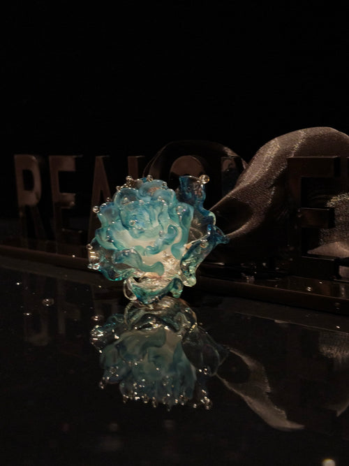 Close-up of handcrafted blue Liuli glass rose floral pendant, ocean blue petals with crystal clear details against black background