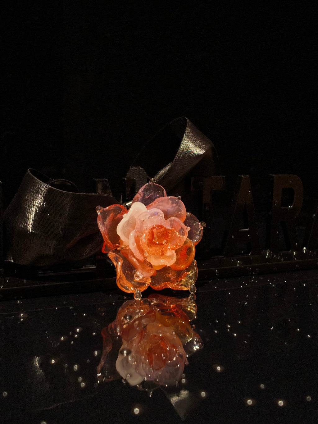 Close-up of handcrafted pink Liuli glass rose pendant, blush pink petals with gold accents and crystal clear details against black background