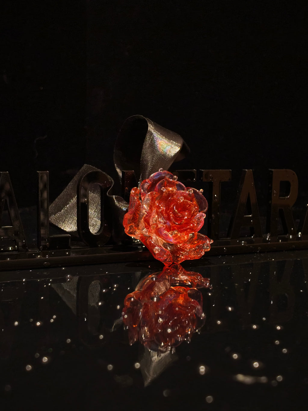 Close-up of handcrafted red Liuli glass rose pendant, deep crimson petals with crystal clear details against black background