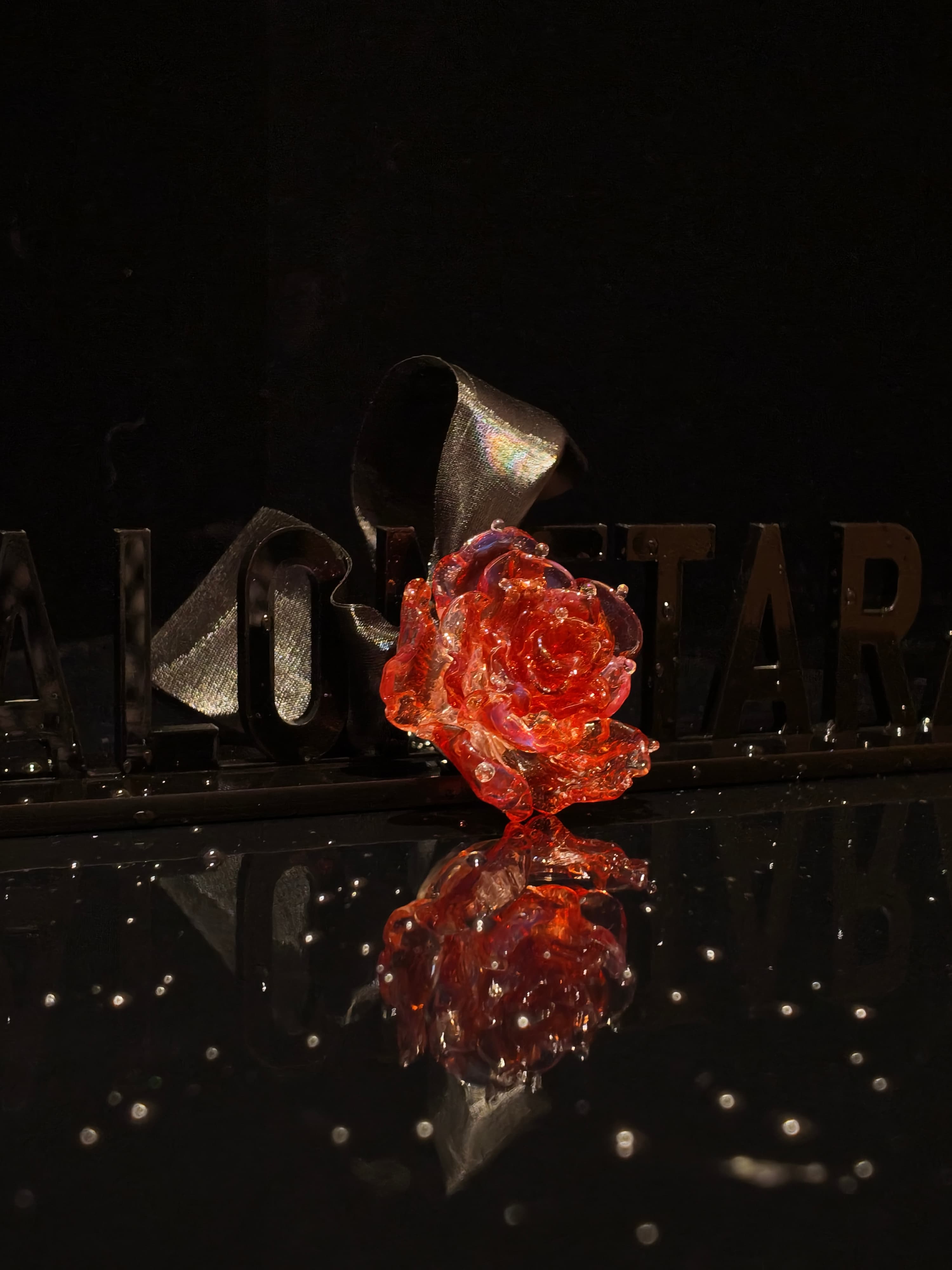 Close-up of handcrafted red Liuli glass rose pendant, deep crimson petals with crystal clear details against black background