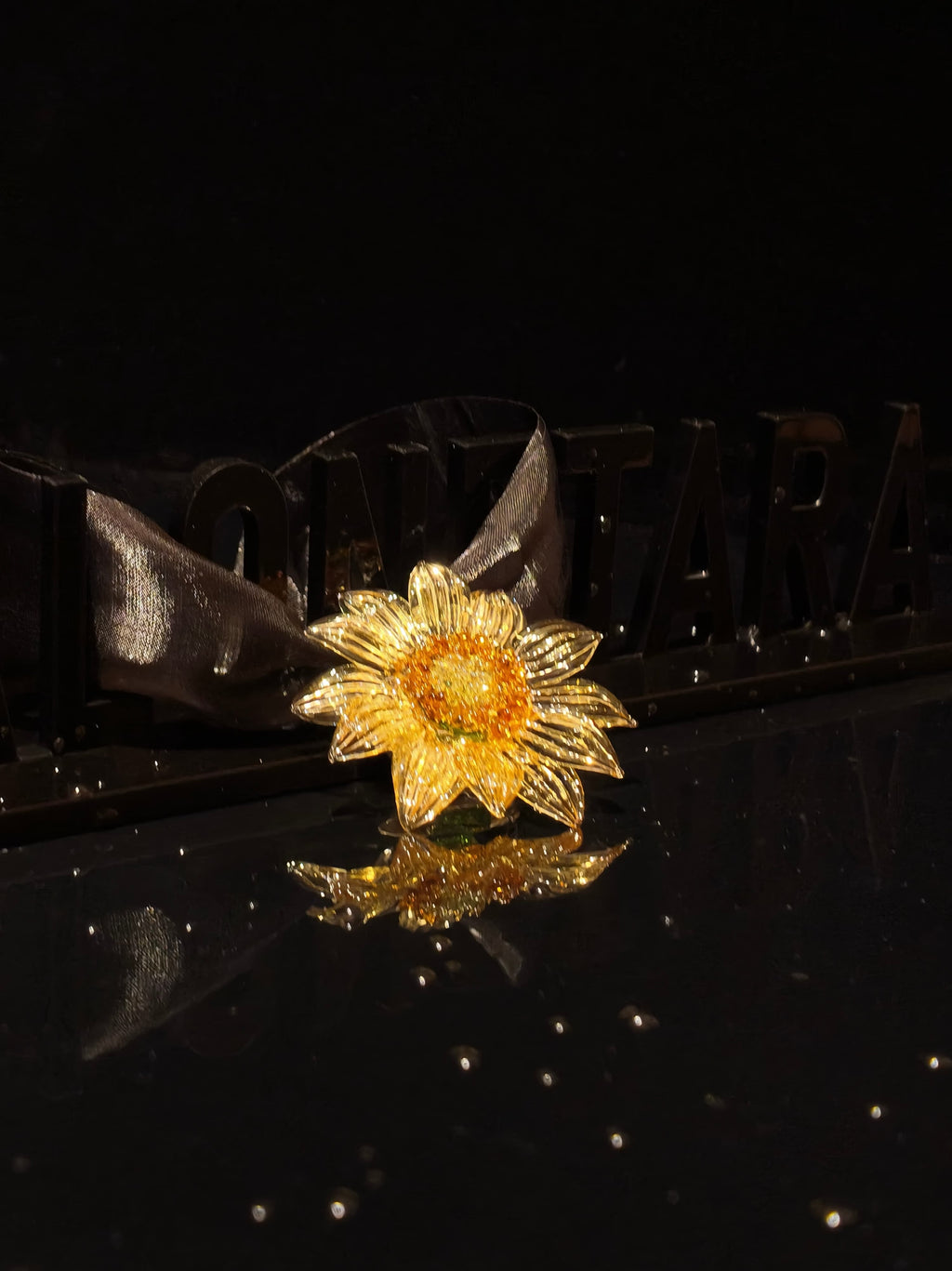 Close-up of handcrafted yellow Liuli glass sunflower floral pendant, bright yellow petals with gold accents and crystal clear details against black background