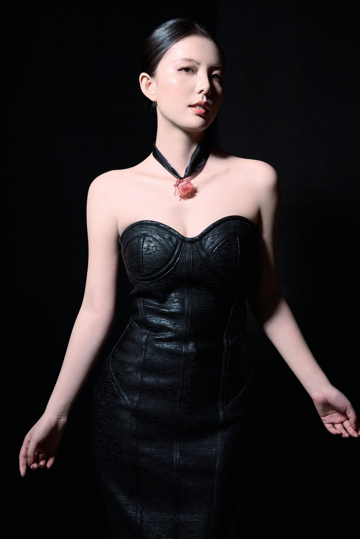 Model in black strapless leather skirt with updo hair, chin slightly raised, slight side profile gazing at camera wearing Pink Lady Liuli Glass Rose Choker Necklace against solid black background