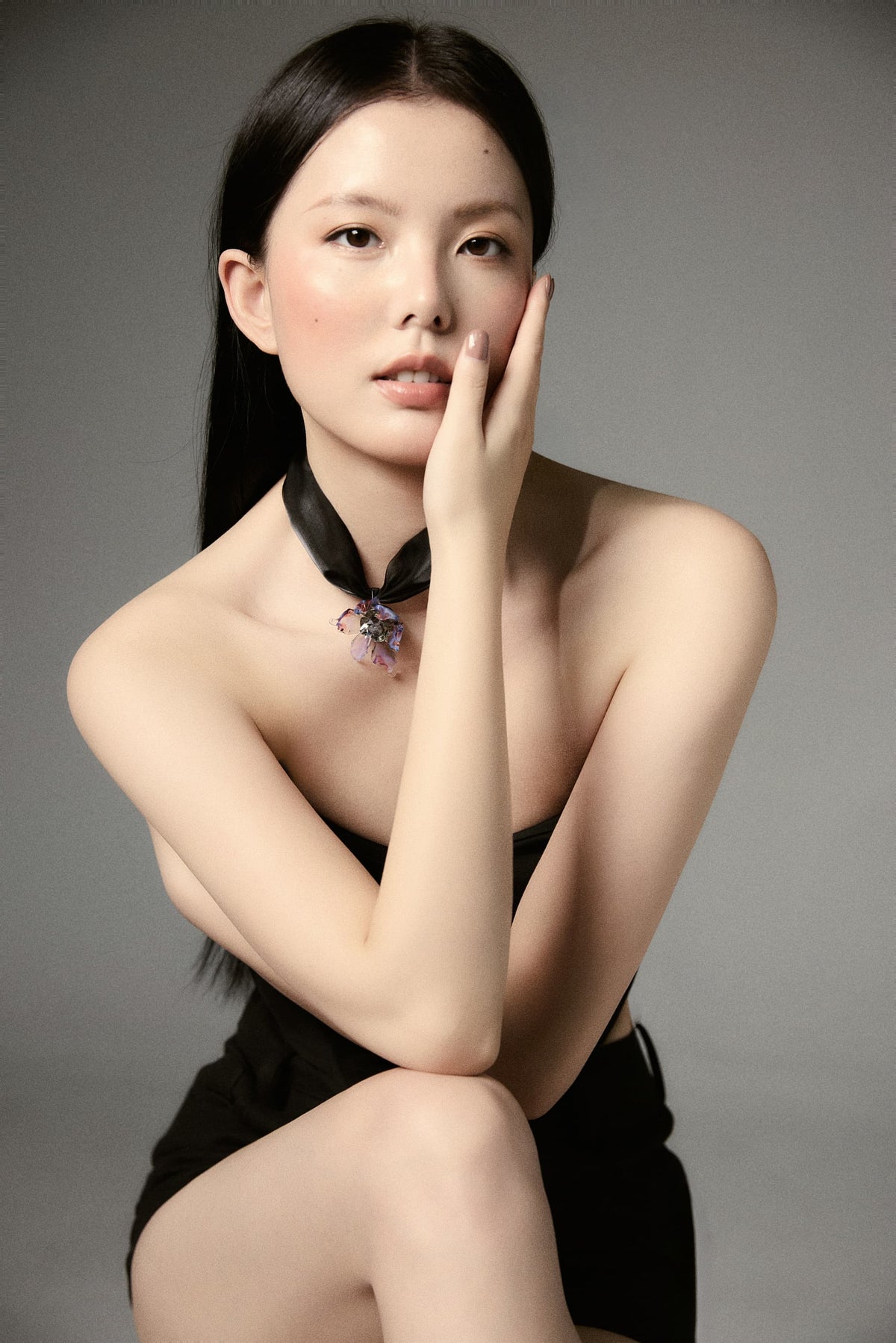 Model in black shorts and black strapless top, seated with one arm wrapped around herself and one hand cradling her face, long straight black hair, gazing directly at camera wearing Queen Purple Blue Liuli Glass Orchid Choker Necklace